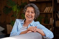 A senior lady sitting on a couch smiling.